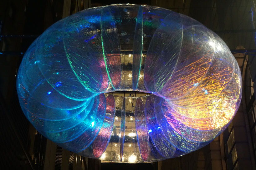 floating oculus installation shimmers in shifting chromatic light above brooklyn's streets