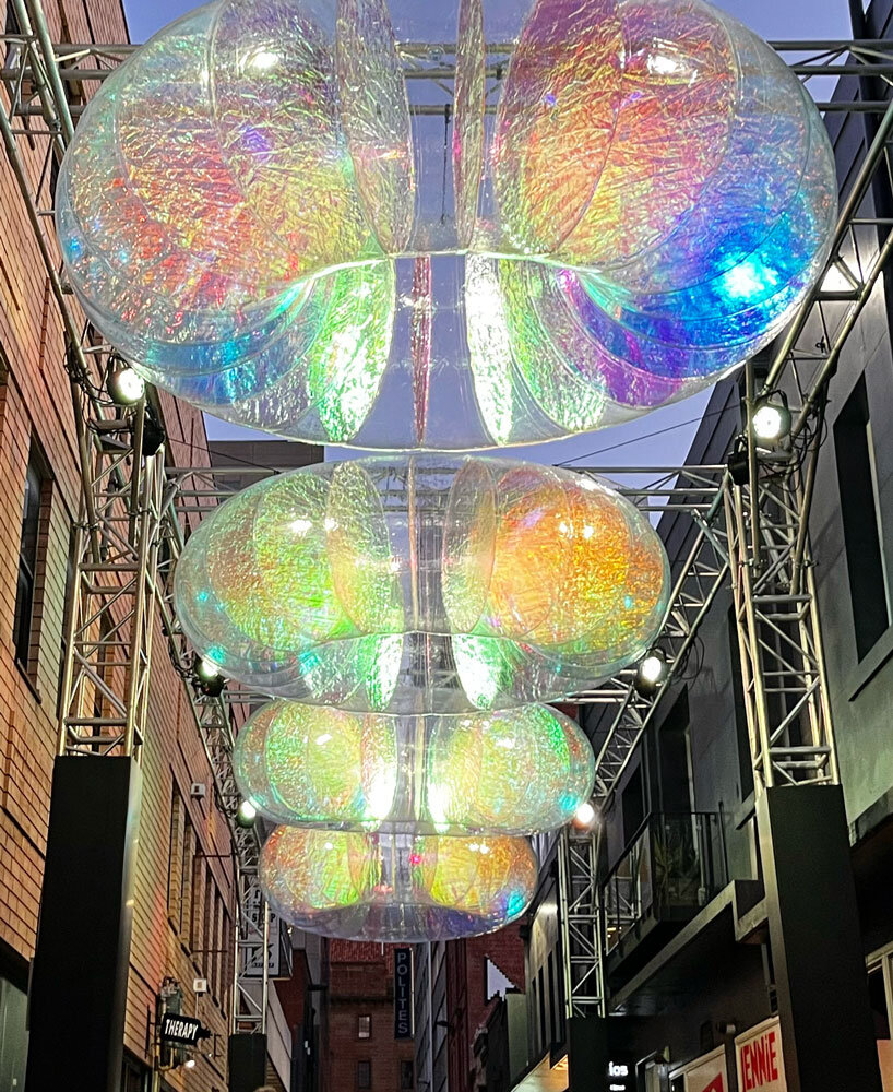 floating oculus installation shimmers in shifting chromatic light above brooklyn's streets