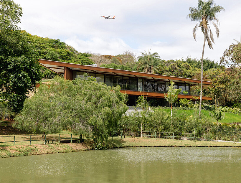 La casa de TETRO junto al lago en Brasil desaparece en el horizonte bajo techos triangulares de madera