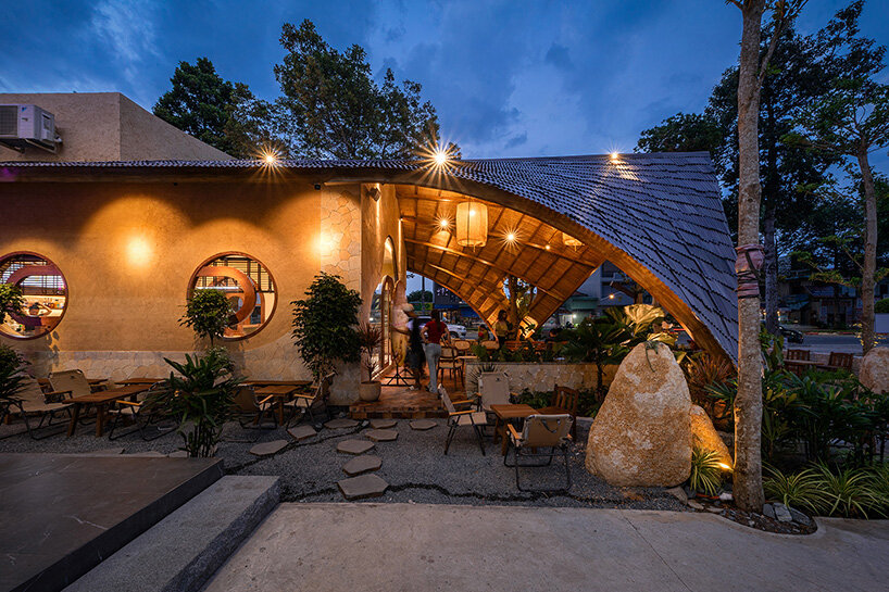 rippling metal roof drapes over interlocking stone volumes of vietnamese caf&eacute;