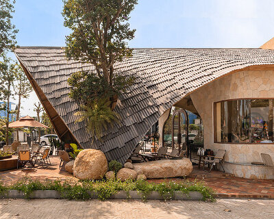 rippling metal roof drapes over interlocking stone volumes of vietnamese café
