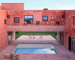 square openings punctuate the facade of courtyard-centric red house in albania