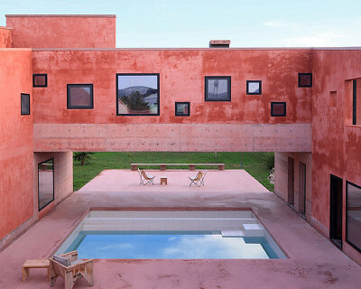 square openings punctuate the facade of courtyard-centric red house in albania