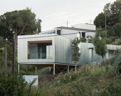 metallic house 144º rises on steel stilts above hillside near barcelona