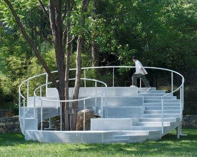 steel rings and stepped platforms spiral around trees in landscape gathering installation