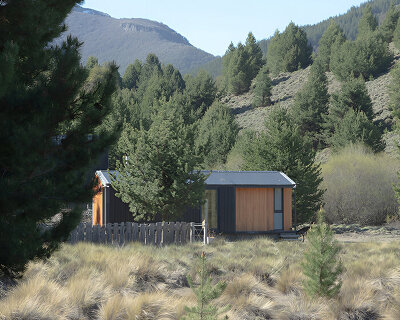 a modular cabin stands between river, forest, and mountains in argentine patagonia