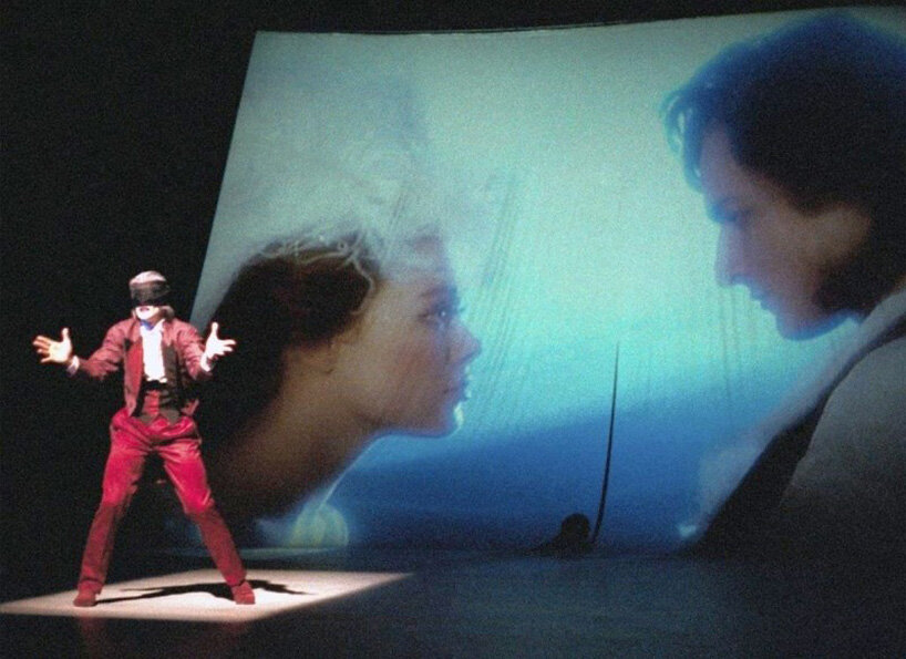a live performer appears alongside a large projected image of two faces