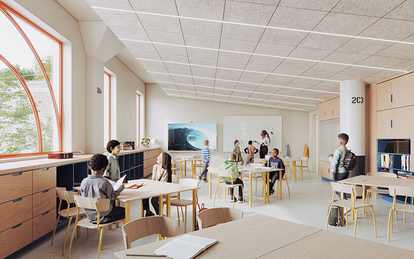 Students work around tables in a bright classroom with large windows, light wood storage cabinets, and yellow chairs